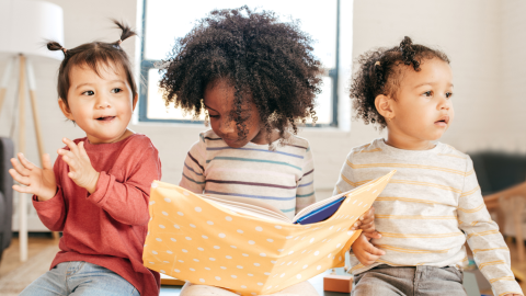 Three children sit together with a book