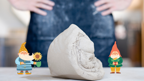 A lump of clay on a table in front of a person wearing an apron with their hands on their hips. To the right and left of the clay are illustrated garden gnomes.