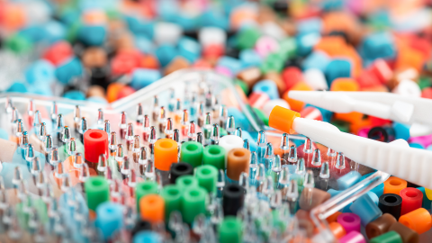 Colorful beads being placed onto a star-shaped peg board with tweezers