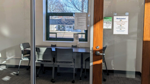 Looking into the door and windows, there is a rectangular table surrounded by four chairs in the quiet study room 2. There is also a window to the park.