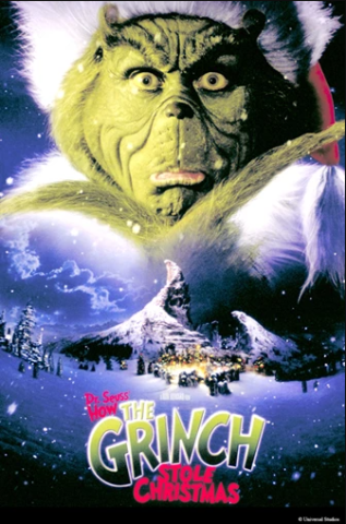The face of a green and fuzzy creature wearing a Santa hat and looking quizzical appears above the landscape of a steep, snowy mountain looming behind a brightly lit and decorated town covered in snow.