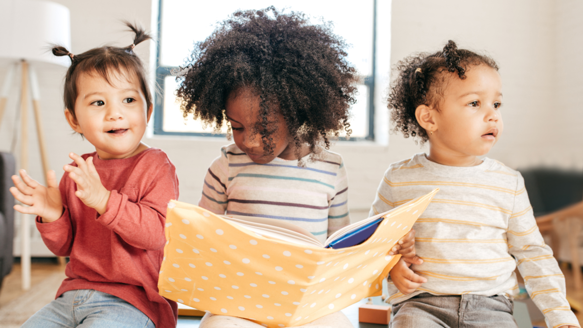 Three children sit together with a book