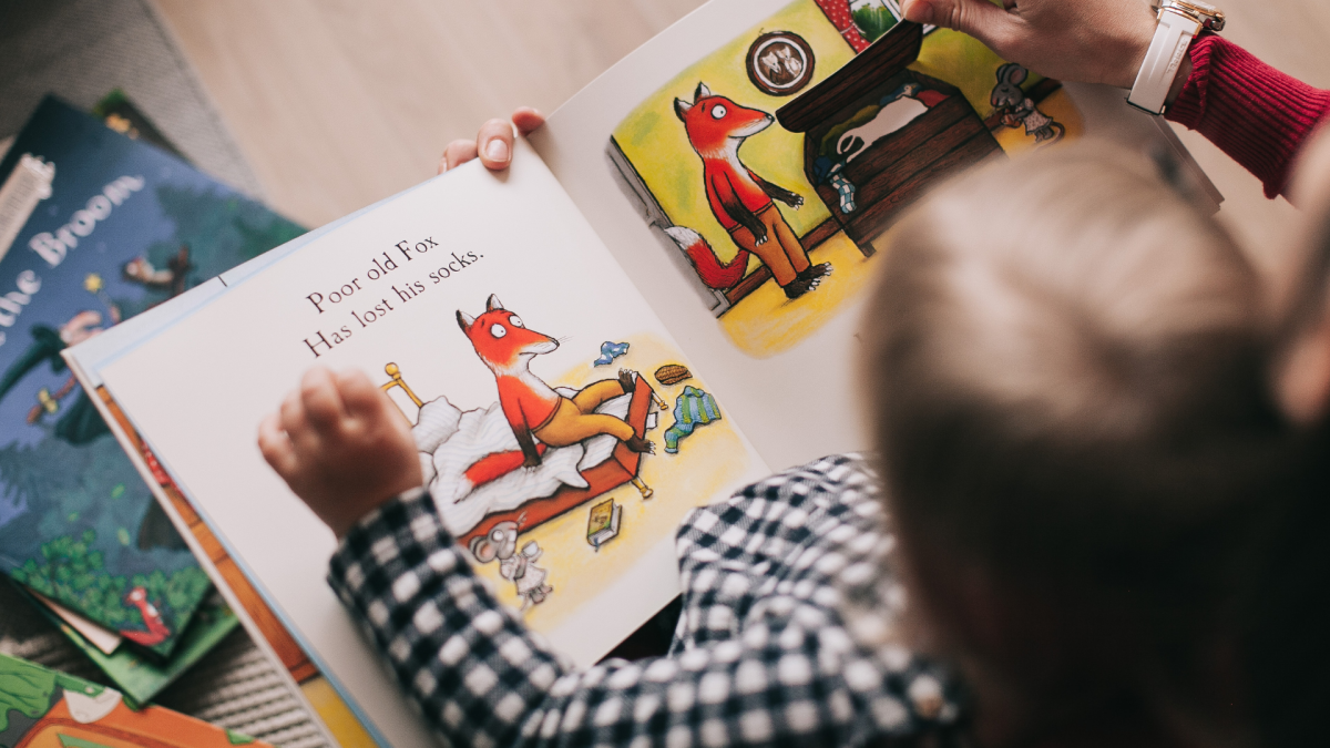 Image from behind a baby sitting on an adult's lap reading a book