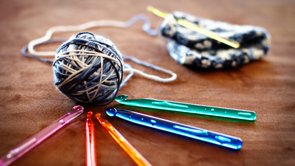 A ball of yarn connected to a started crochet project encircled by colorful crochet hooks